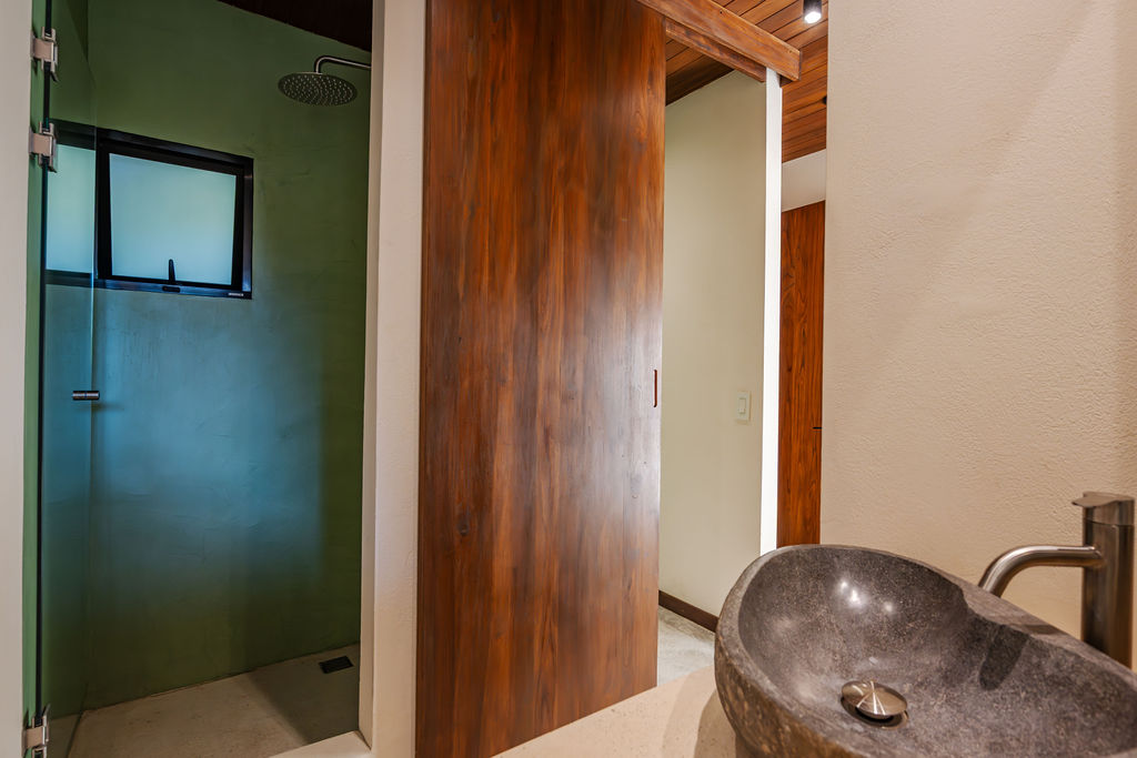 Walk-in shower in green plaster behind a glass screen, with a teak sliding door alongside
